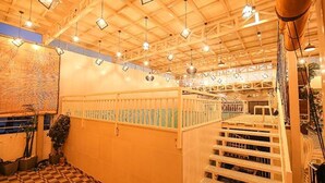 Une pièce avec un plafond haut, des poutres en bois et des luminaires suspendus. Un escalier avec une rampe mène à un niveau supérieur.