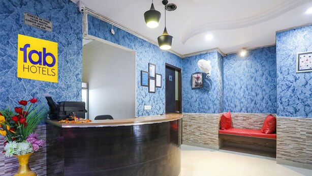 A hotel reception area with a marble wall, a reception desk, a seating area with red cushions, and a sign for 'fab hotels'. - Fabexpress Chef'S House (Gurugram)