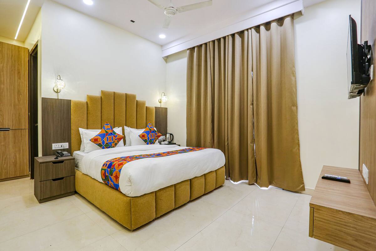 A hotel room with a bed, nightstand, TV, and curtains.