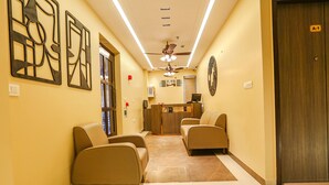 A reception area with a desk, two chairs, a ceiling fan, and a clock on the wall. - Fabhotel Vishesh Villas (New Delhi)