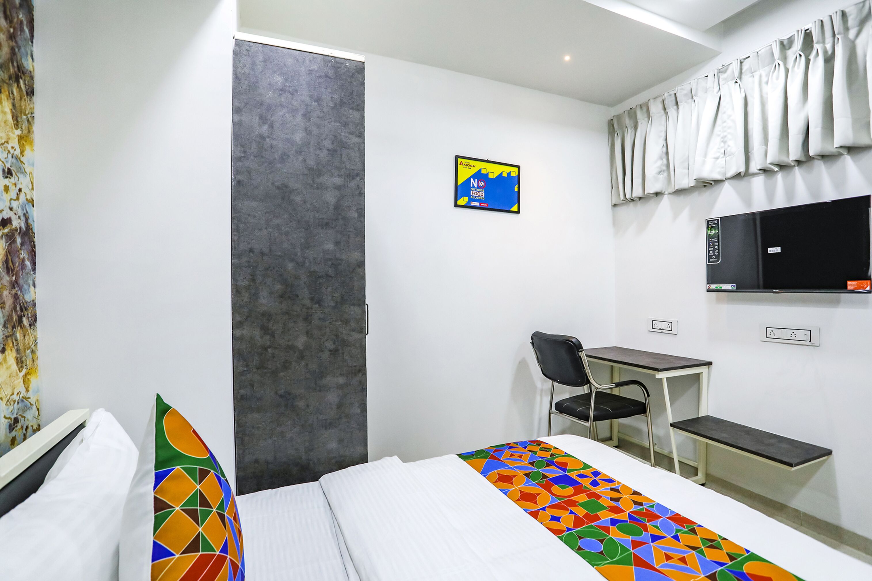 A hotel room with a bed, a desk, a chair, a TV, and a painting on the wall.