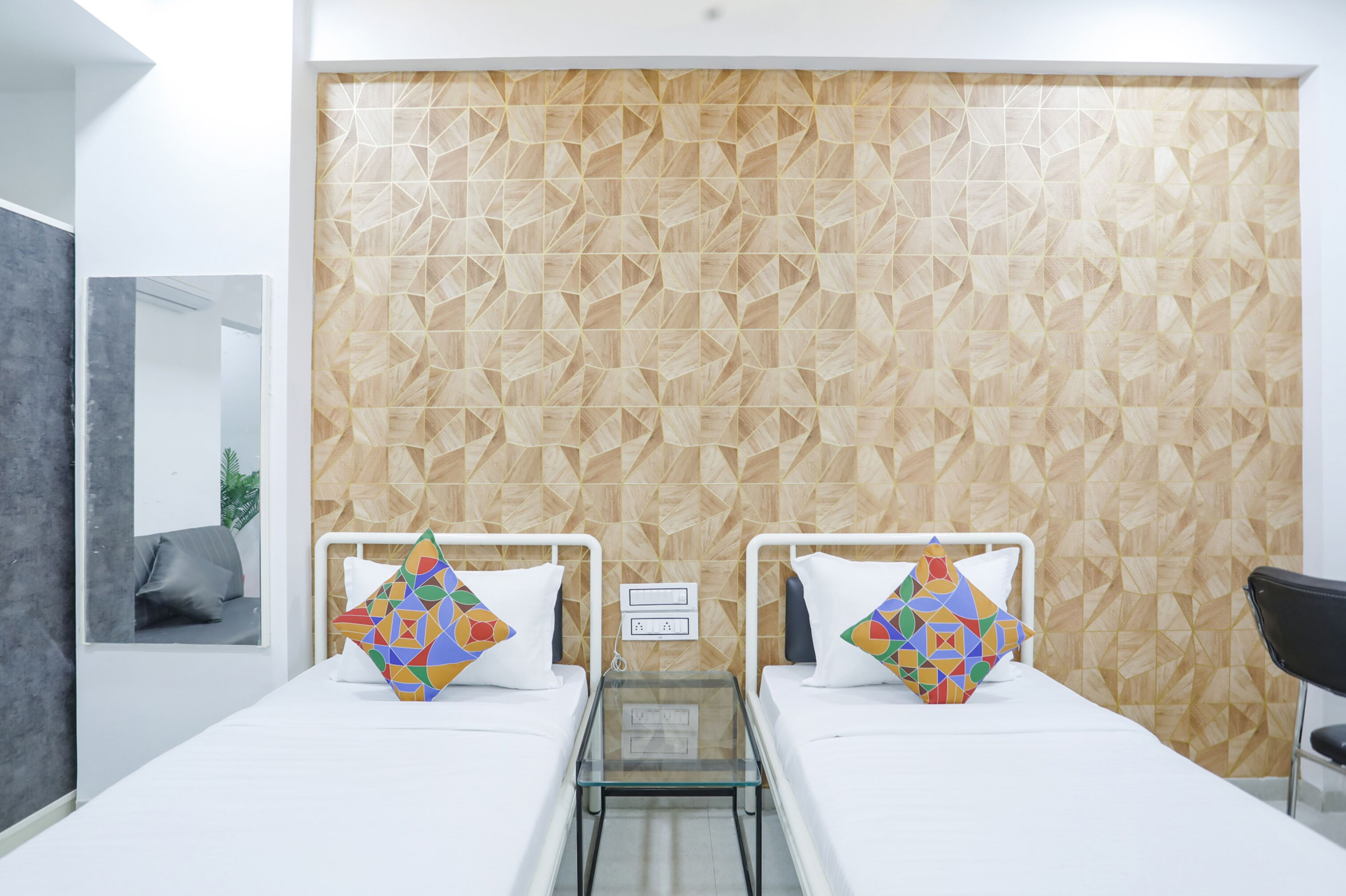 Ein Hotelzimmer mit zwei Betten, einem Glastisch und einer Wand mit geometrischem Muster.