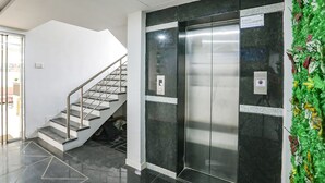 A modern elevator with a control panel, a staircase with metal railings, and a wall with a green decorative plant. - Fabhotel Amogh Stay Inn (Nagpur)