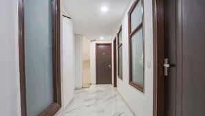 A corridor with marble flooring, wooden doors, and a ceiling light. - Fabhotel 24&7 (New Delhi)