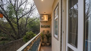 A balcony with a view of trees, a ceiling fan, and potted plants. - Fabhotel 24&7 (New Delhi)
