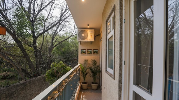 A balcony with a view of trees, a ceiling fan, and potted plants. - Fabhotel 24&7 (New Delhi)