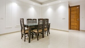 A dining area with a rectangular table and six chairs, a wooden door, and white walls. - Fabhotel 24&7 (New Delhi)