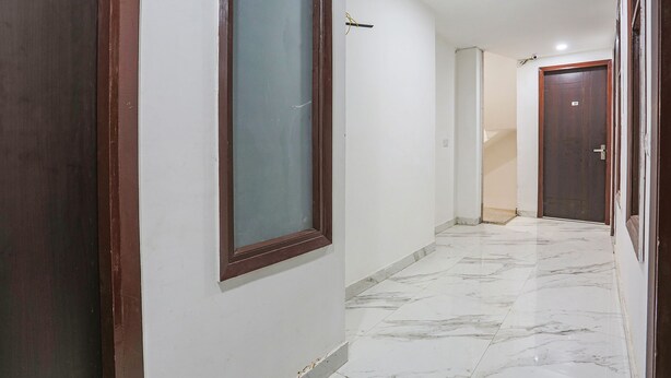 A hallway with a marble floor, a wooden door frame, and a white wall with a window. - Fabhotel 24&7 (New Delhi)