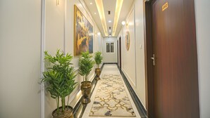 A hallway with a patterned carpet, potted plants, framed artwork, and a door with a number plate. - Fabhotel Relax Inn Palace (Haridwar)