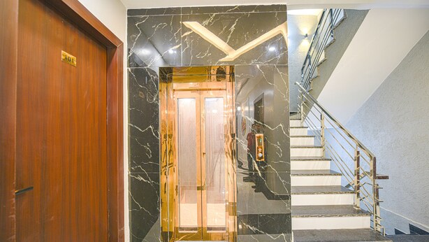 A wooden door with a number plate, a marble wall with a geometric pattern, and a staircase with metal railings. - Fabhotel Relax Inn Palace (Haridwar)
