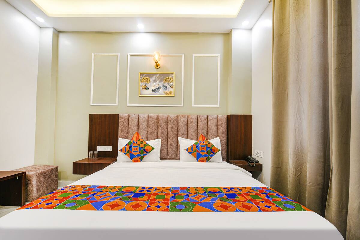 A hotel room with a large bed, two bedside tables, a nightstand, a wall-mounted lamp, and a framed picture above the bed.