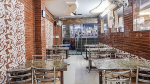 A restaurant with marble-topped tables and chairs, patterned wall designs, and ceiling fans. - Fabhotel Sarwan (Agra)