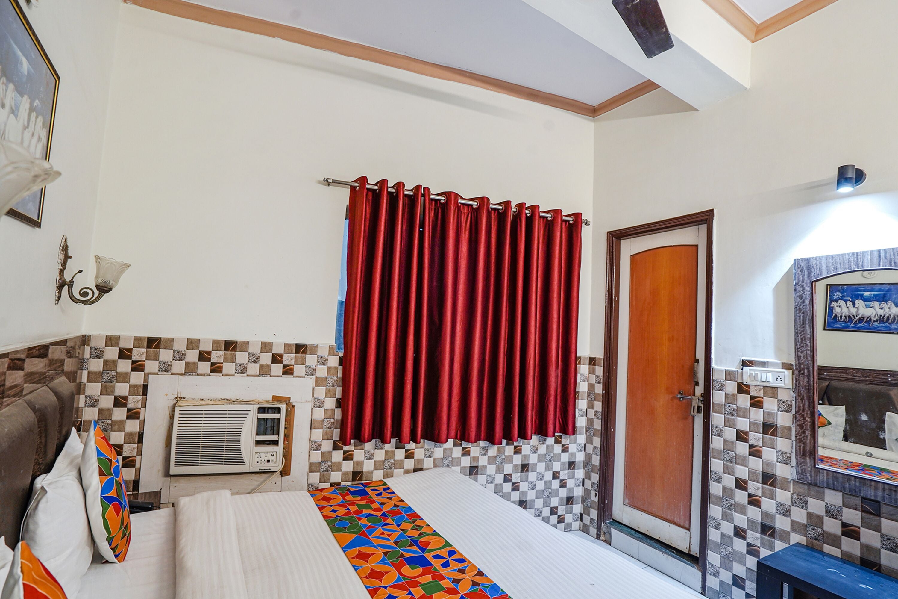 A bedroom with a bed, a red curtain, a wall-mounted air conditioner, and a checkered tile pattern on the walls.