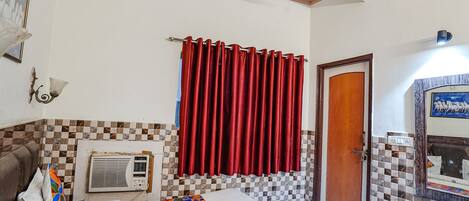 A bedroom with a bed, a red curtain, a wall-mounted air conditioner, and a checkered tile pattern on the walls.