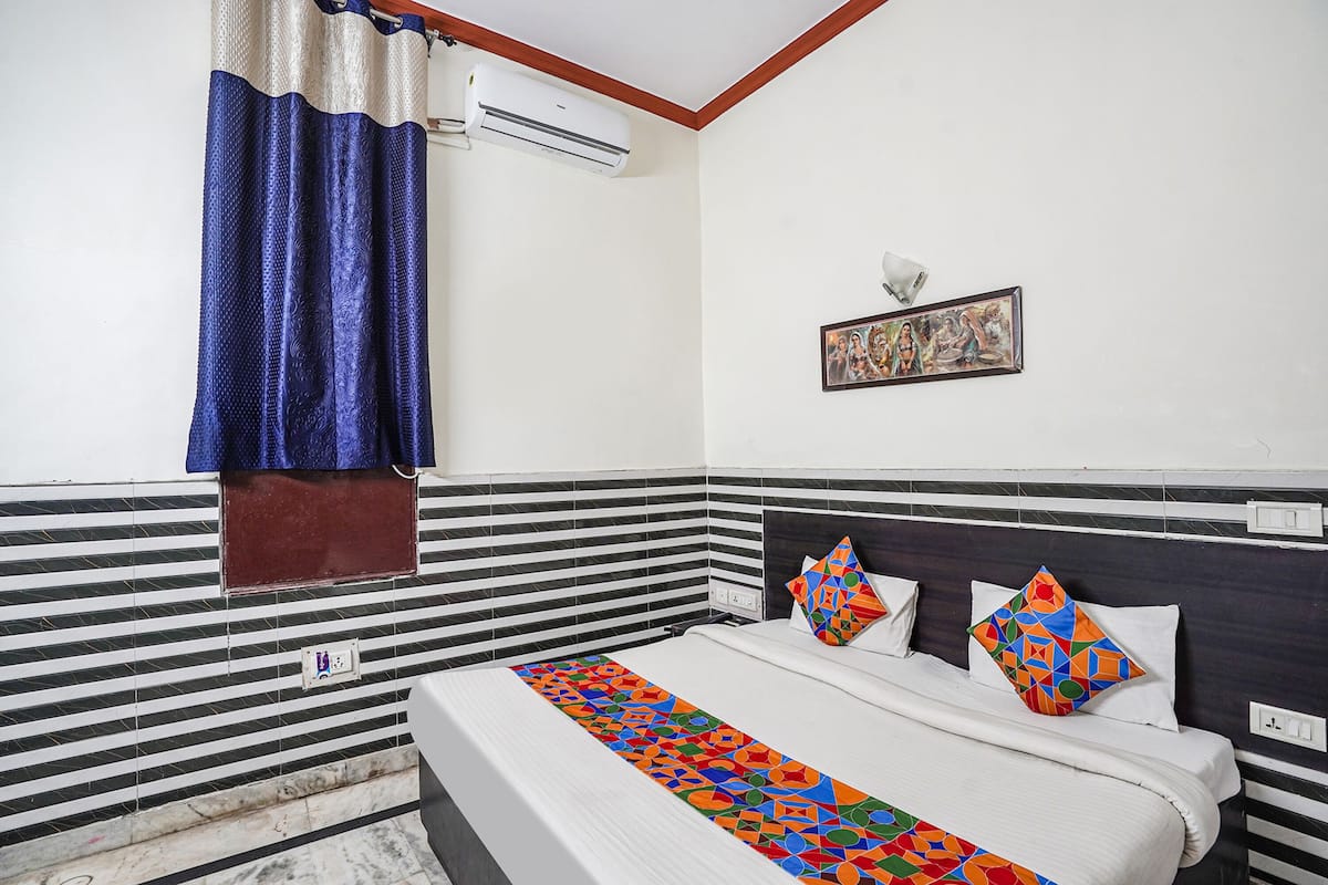 Habitación de hotel con cama, ventana con cortinas, equipo de aire acondicionado, cuadro en la pared y piso de baldosas.