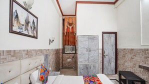 A hotel room with a bed, a bench, a wardrobe, and a bathroom visible through an open door. - Fabhotel Sarwan (Agra)