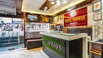 A hotel reception area with a reception desk, a sign for Hotel Sarwan, and an exit sign.