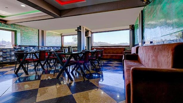 A restaurant with a checkered floor, tables, chairs, and a red sofa. - Fabhotel Hill View (Madikeri)