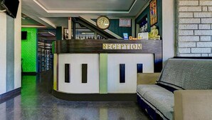 A reception desk with a clock above it, a sofa, and a brick wall in the background. - Fabhotel Hill View (Madikeri)