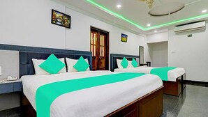A hotel room with two beds, each with white bedding and teal accents, a wooden headboard, a small bedside table with a phone, and a window with curtains. - Fabhotel Hill View (Madikeri)