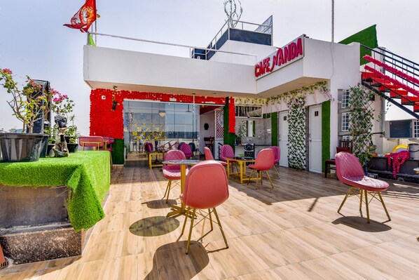 Un café llamado 'Cafe Manda' con mesas al aire libre, una escalera y plantas decorativas.