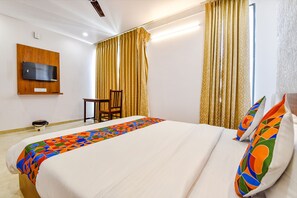 Relax in a cozy space with a neatly made bed, flat-screen TV, and a compact table and chair.