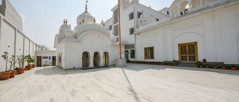 A spacious courtyard with a white building featuring domed structures and a flagpole.