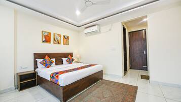 A bedroom with a bed, nightstand, air conditioning unit, and a door leading to another room.