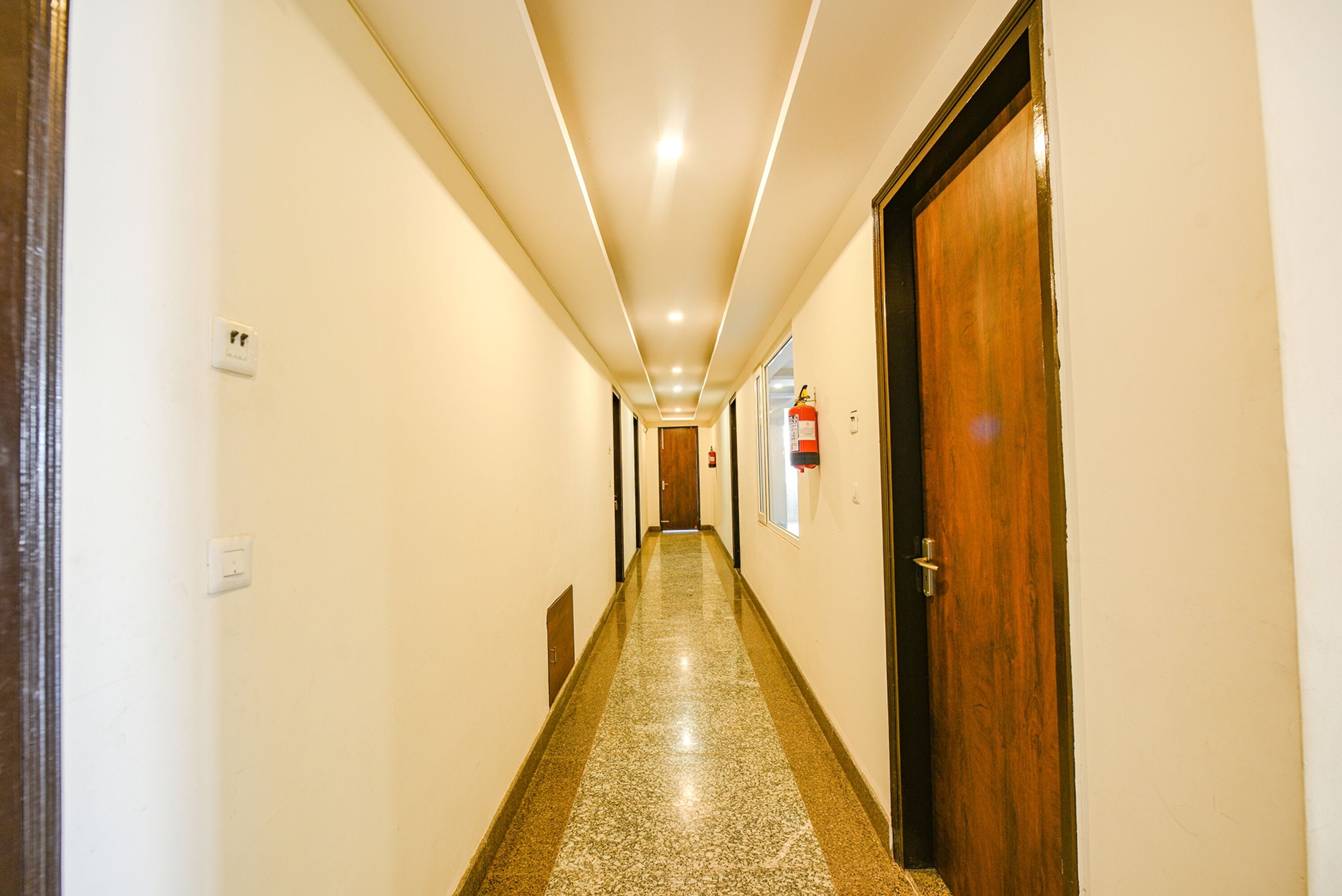 A hallway with a polished floor, a wooden door on the right, and a fire extinguisher on the wall.