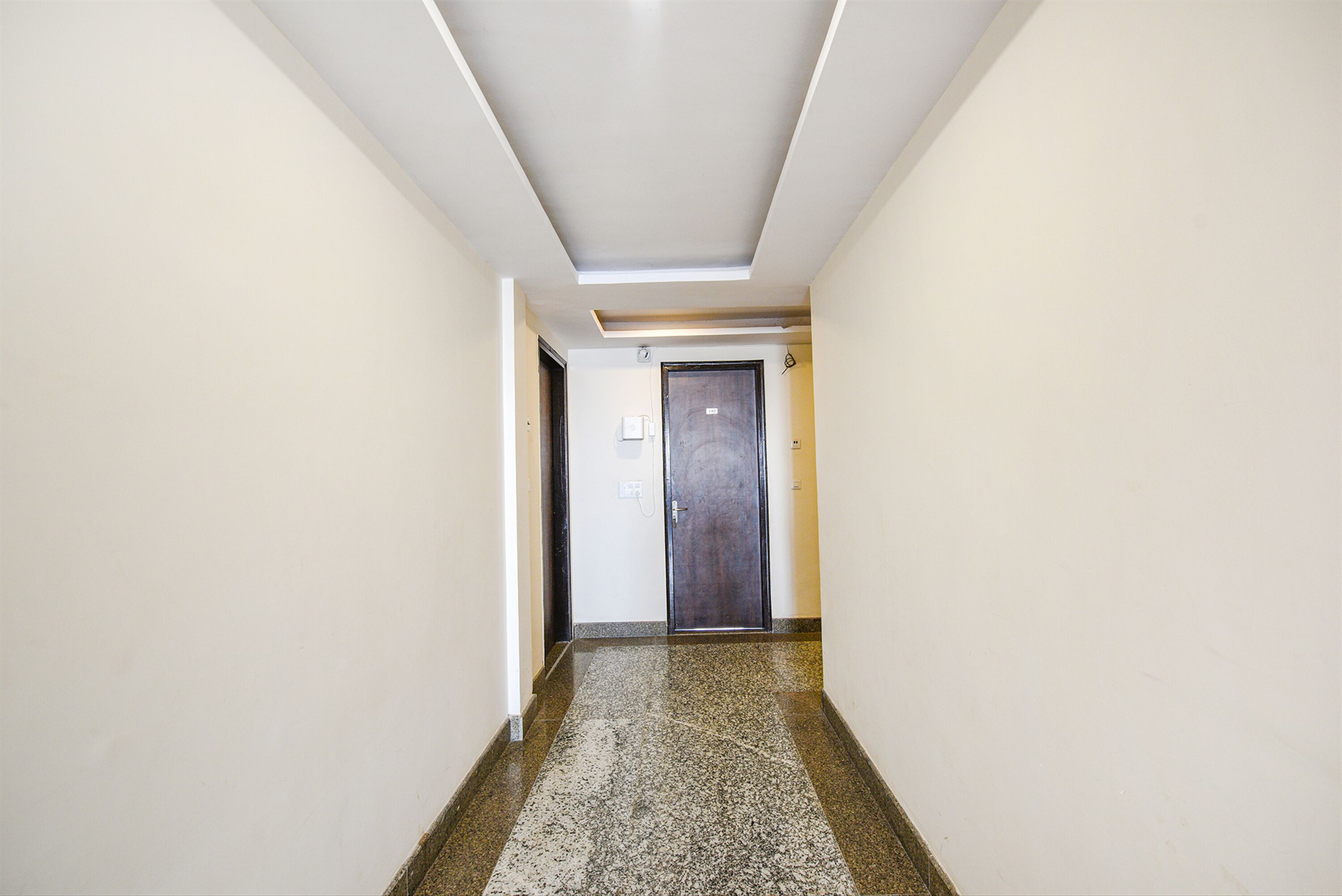Un pasillo con piso pulido, techo con iluminación empotrada y una puerta al final.