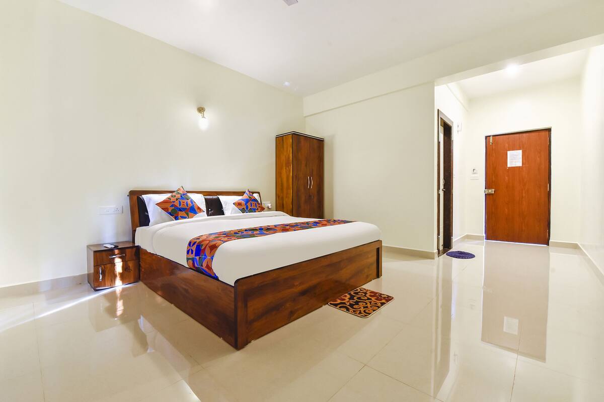 Quarto de hotel moderno com cama de madeira, mesa de cabeceira, guarda-roupa e porta do banheiro.