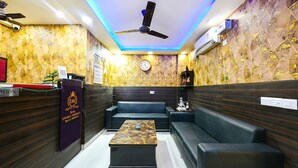 Un espace d’accueil d’hôtel comprenant un comptoir de réception, une horloge, un ventilateur de plafond et des sièges.