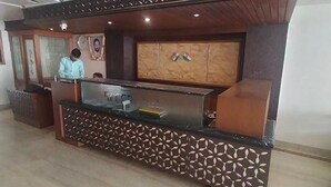 A reception desk with a patterned design, a wooden cabinet with flags, and a security camera above. - Fabhotel Satlaj (Raipur)