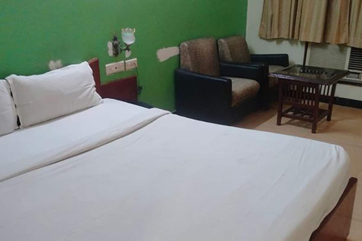 Quarto de hotel com uma cama grande, uma cadeira, uma mesinha e uma parede verde.