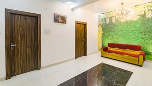 Un passadís amb dues portes de fusta, un sofà groc amb una manta vermella i una paret amb motius florals verds.