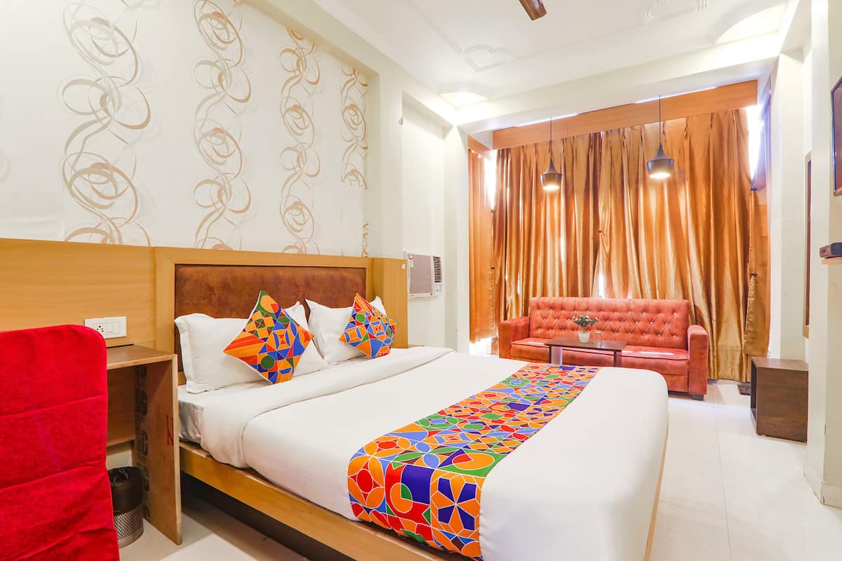 A hotel room with a large bed, a red armchair, a wooden nightstand, and a red chair.