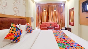 Habitació d'hotel amb un llit gran, un sofà vermell i una televisió penjada a la paret.