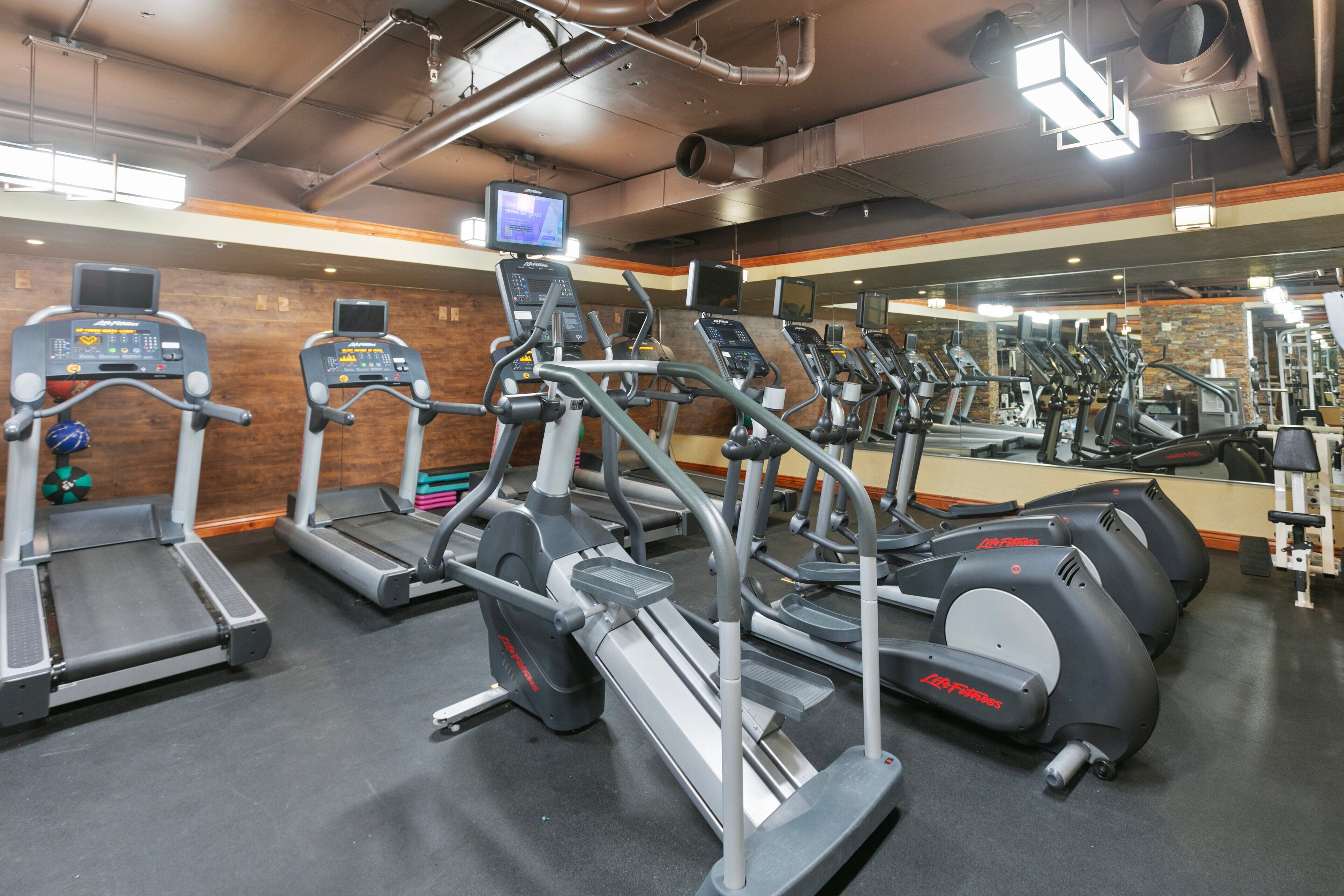 A gym with multiple treadmills, ellipticals, and a mirrored wall.
