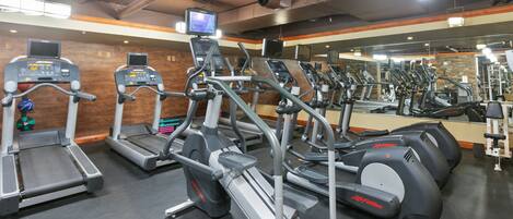 A gym with multiple treadmills, ellipticals, and a mirrored wall.