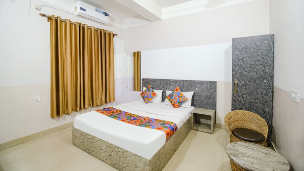 A hotel room with a bed, a nightstand, a wicker chair, and a marble wall. - Fabexpress Sai Villa (Guwahati)