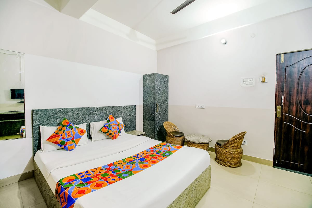 A modern hotel room with a large bed, a marble headboard, a small table, wicker chairs, and a dark wooden door.