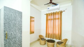 A bathroom with a marble wall, two wicker chairs, a round metal basin, and a ceiling fan. - Fabexpress Sai Villa (Guwahati)