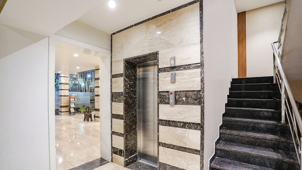 A modern elevator with a marble wall, a staircase with a metal railing, and a polished floor. - Fabhotel Prime Mahendra (Raipur)