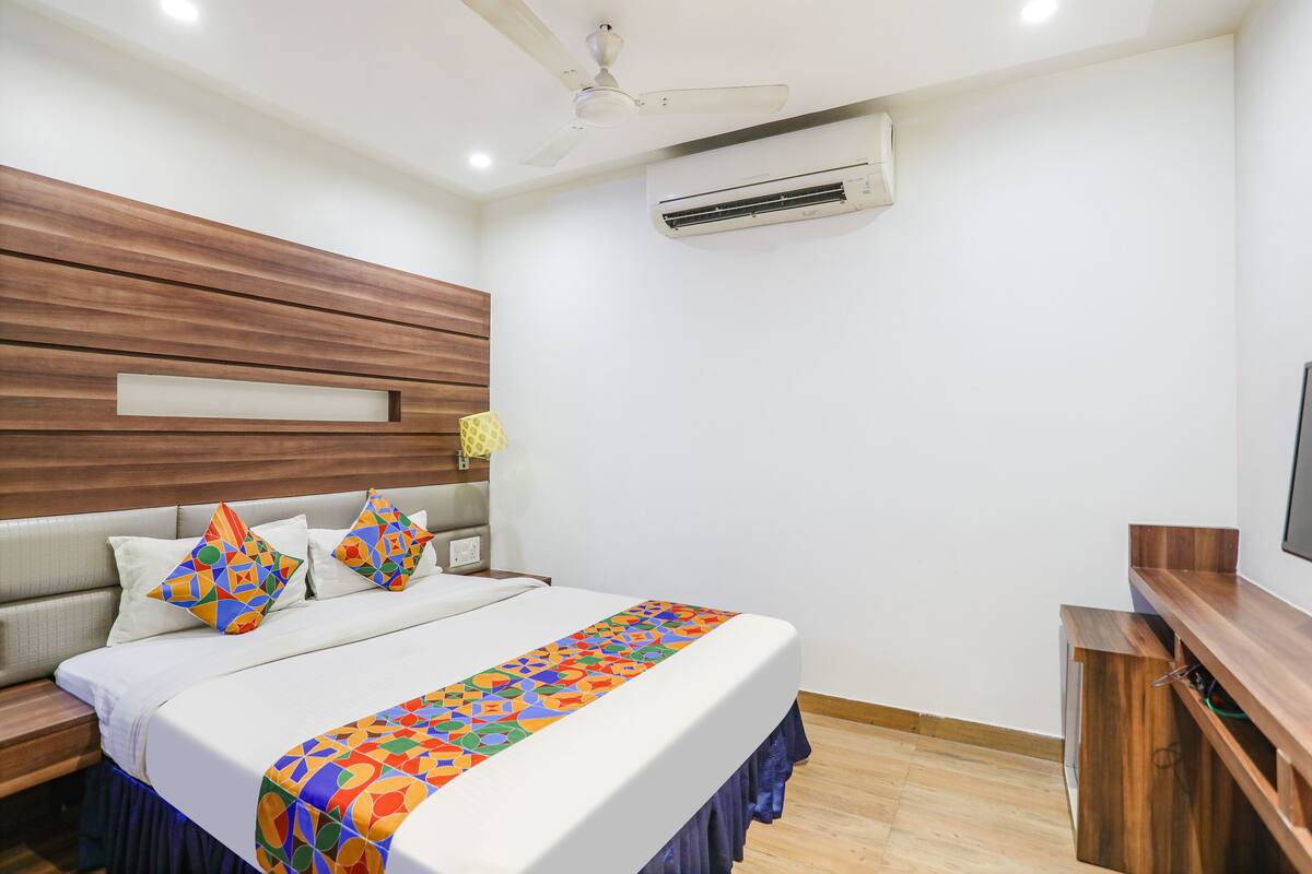 A hotel room with a bed, wooden headboard, air conditioning unit, and a TV on a wooden stand.