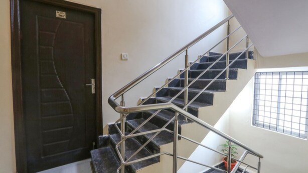 Uma escadaria com grades de metal, uma porta de madeira escura com uma placa de identificação e uma janela com grade metálica.
