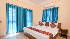 Quarto de hotel com uma cama grande, cortinas, ar condicionado e uma mesa de cabeceira.
