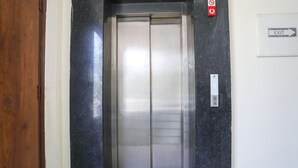 An elevator with a metallic interior, a wooden door frame, and a wall-mounted exit sign. - FabHotel Star Corporate Suite I (Gurugram)
