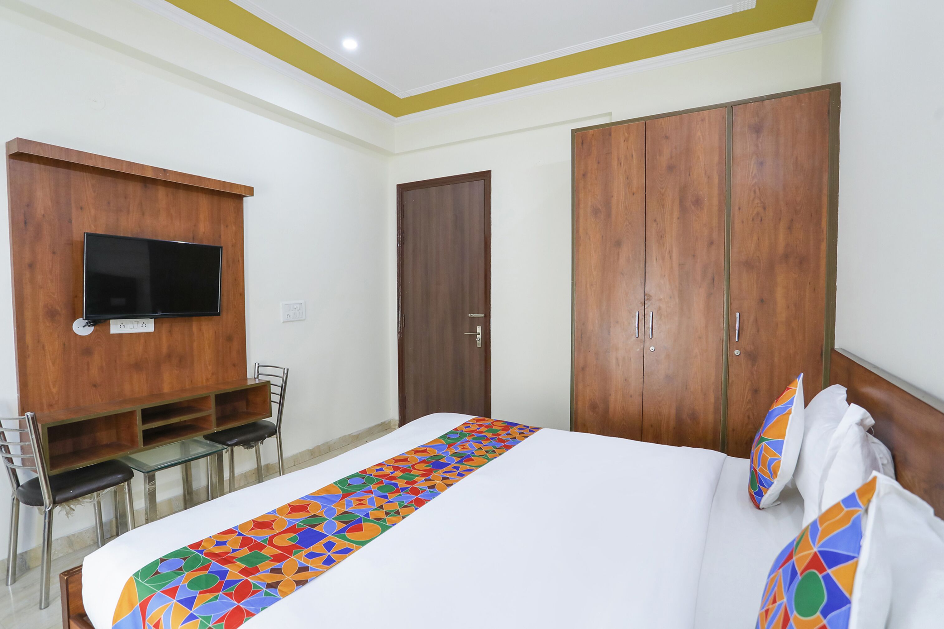 Ein Hotelzimmer mit einem Bett, einem an der Wand montierten Fernseher, einem Schreibtisch mit Stühlen und einem Kleiderschrank.