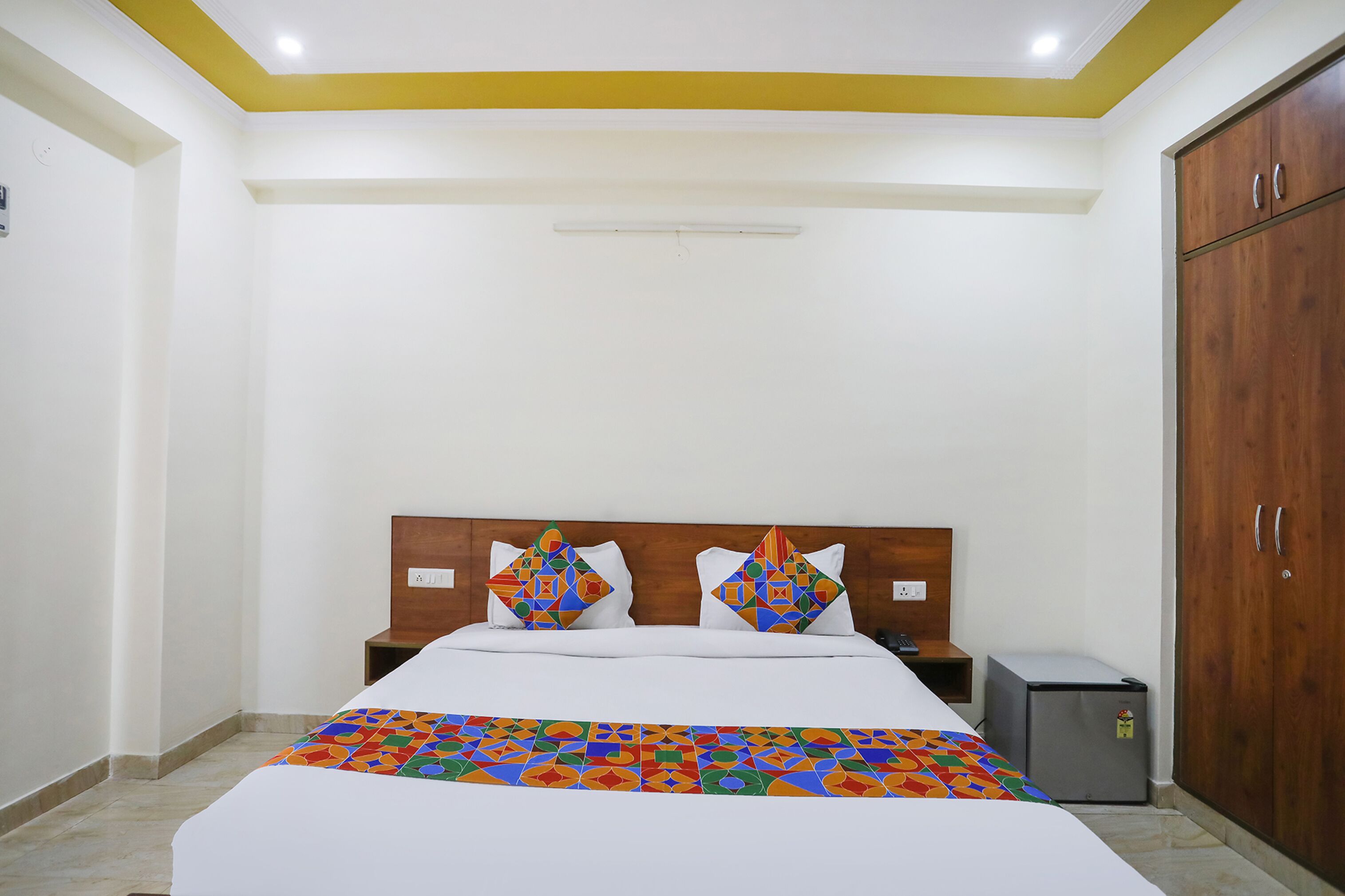 Quarto de hotel com cama, mesa de cabeceira, guarda-roupa e pequeno frigorífico.