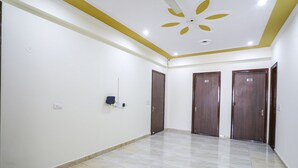 A spacious room with a tiled floor, a ceiling fan, and three wooden doors. - FabHotel Star Corporate Suite I (Gurugram)